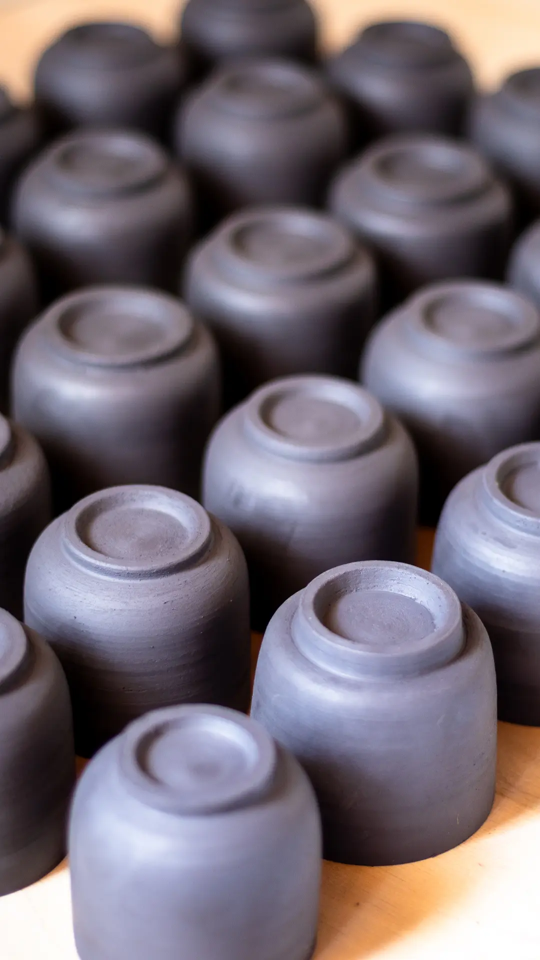 Freshly trimmed black stoneware espresso cups showing detailed foot rings, artisan pottery studio process.