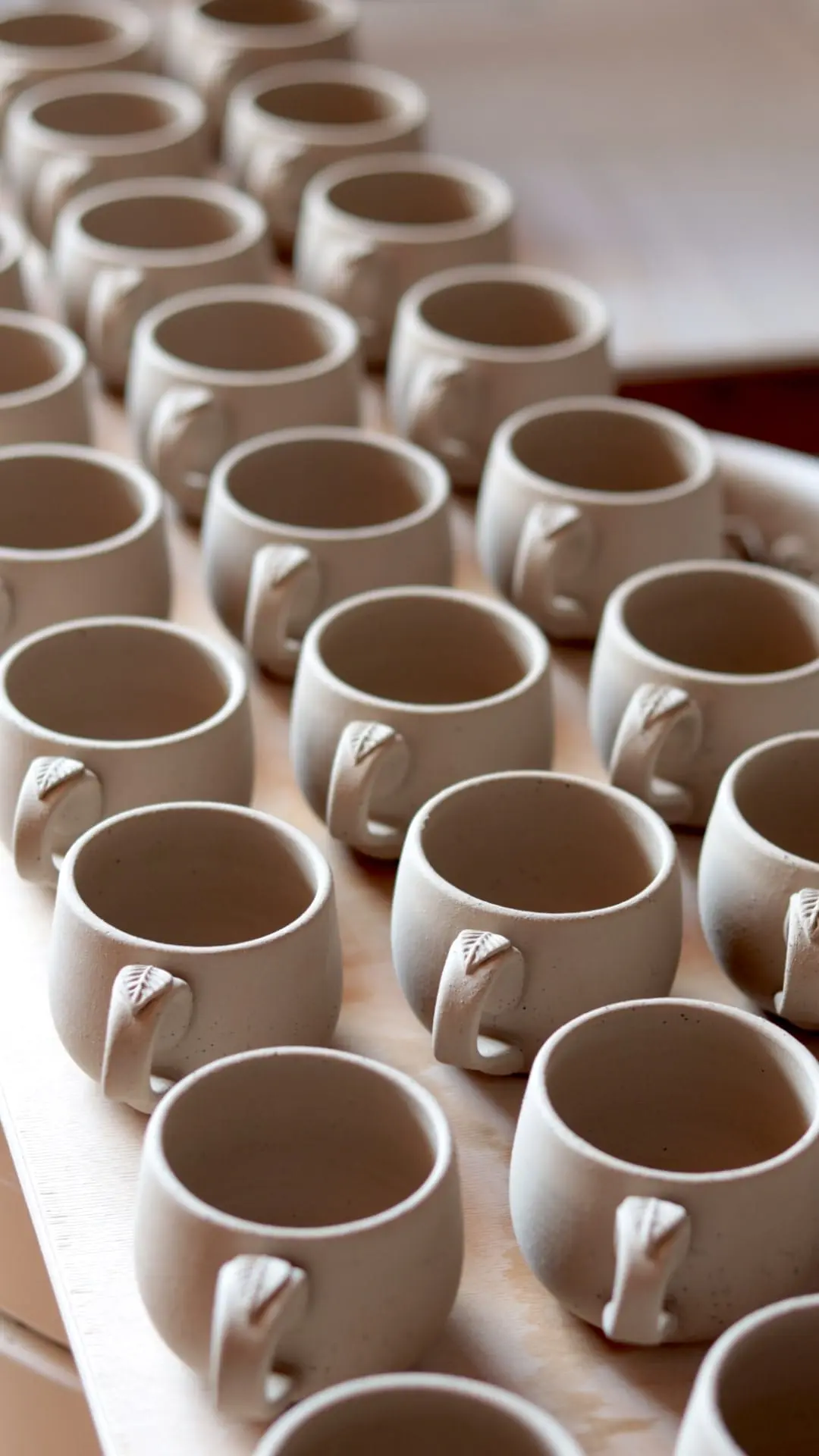 A collection of hand-thrown stoneware espresso cups with delicate leaf-shaped handles, artisanal pottery studio.