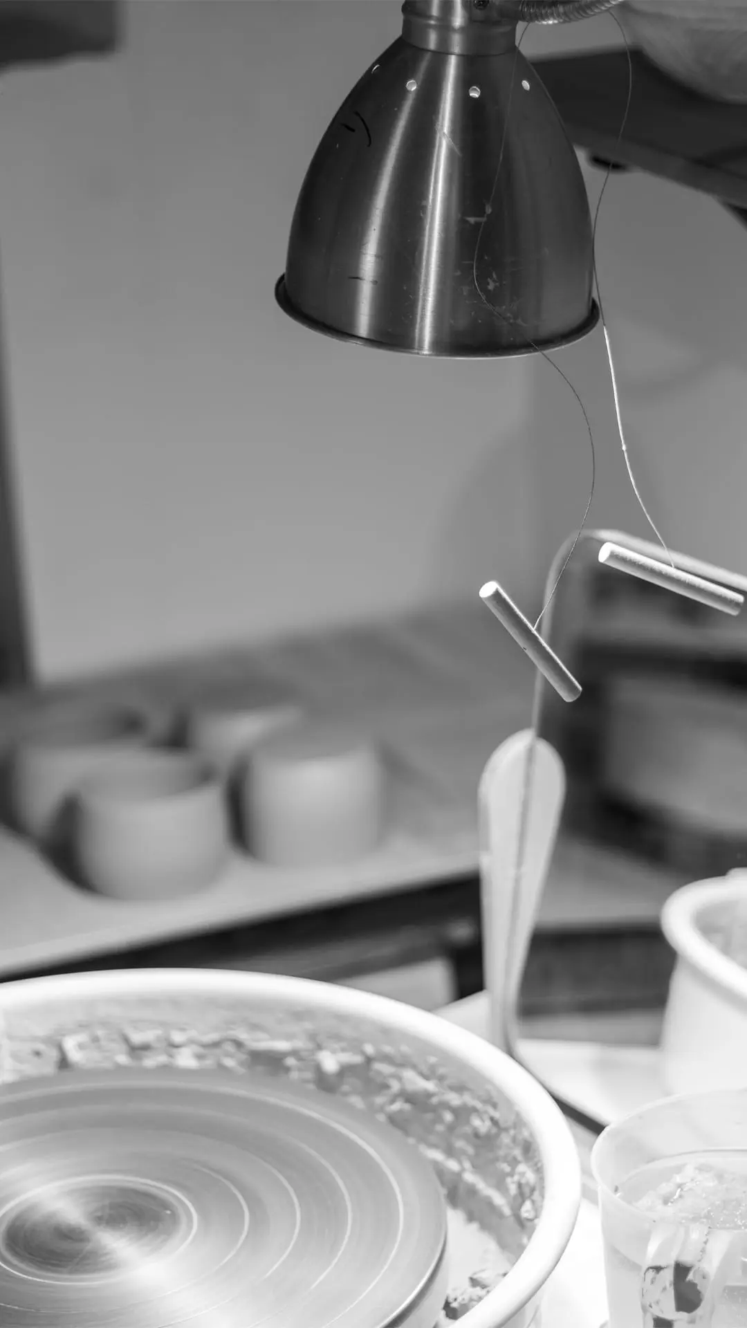 A black and white view of a potter's wheel under a studio lamp at night by Seyma Ates.