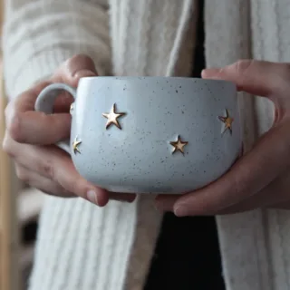 Handmade white stoneware mug with gold stars held in hands, cozy pottery