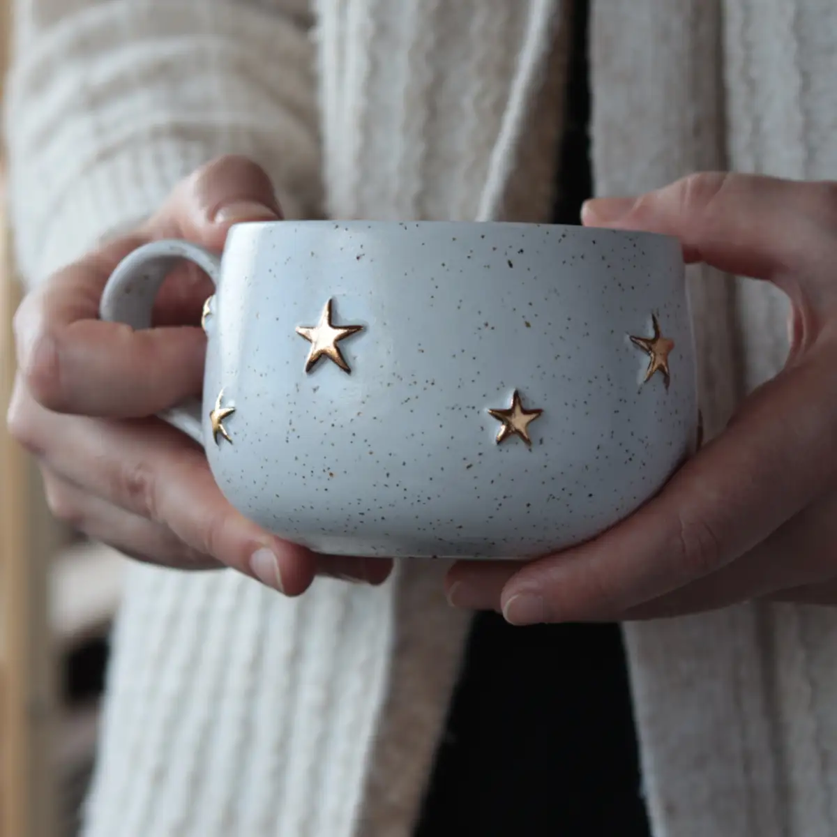 Handmade white stoneware mug with gold stars held in hands, cozy pottery