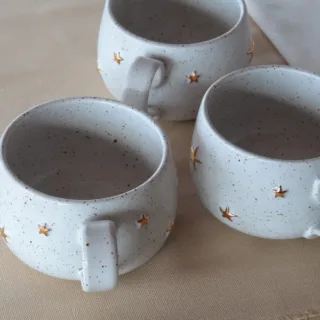 White stoneware mugs with gold star details, handmade ceramic, top view